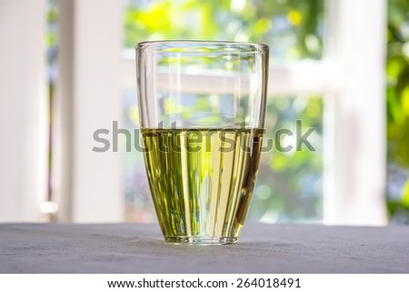 Glass with olive oil placed on a table against the window overlooking the garden.