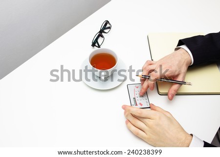 Businessman counting on calculator with cup of tea on white background.