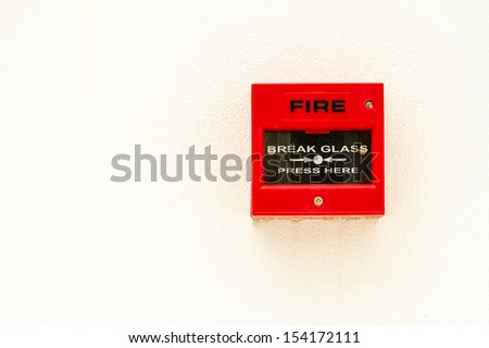 Red fire alarm switch on white concrete wall.