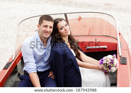 Beautiful stylish newlyweds sitting in a boat on the beach. Gentle bride and handsome groom by the sea.