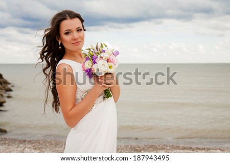 Gentle bride with long hair and a beautiful bouquet on the beach.