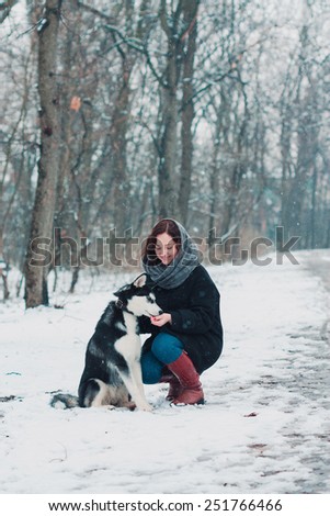 Young woman with husky dog in the winter park. Snow is falling in the forest.