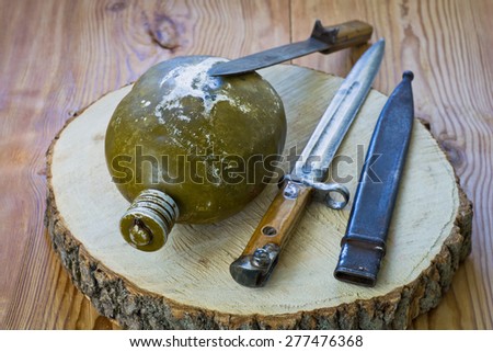 The old army knives and water bottle on a wooden background