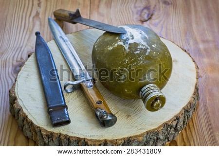 The old army knives and water bottle on a wooden background