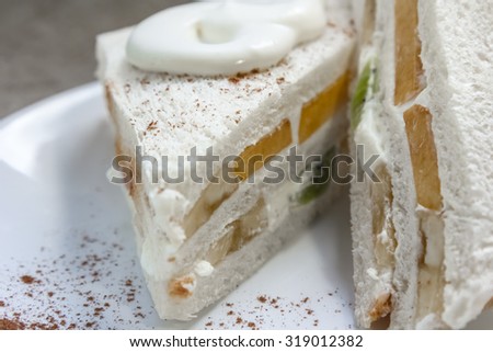 Sweet sandwich with fresh cream, kiwi, peach and cinnamon on a white plate