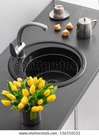 Granite kitchen sink with mixer tap, yellow tulips in the foreground and a cup of coffee in the background