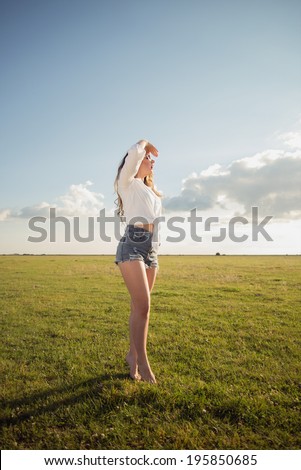 Beautiful woman with sexy legs on grass shoe less watching the sun with her hand above her eyes wearing sunglasses