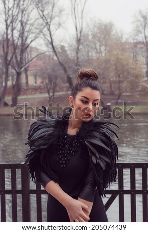 Gorgeous woman wearing a Black Swan feather Collar and a very sexy fashion tight dress with leather sleeves. Portrait