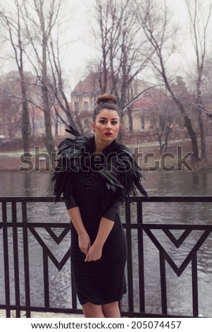 Gorgeous woman wearing a Black Swan feather Collar and a very sexy fashion tight dress with leather sleeves at the river side