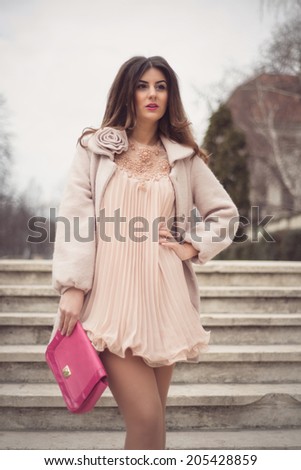 Fashion shoot of an elegant woman wearing a sexy nude dress holding a pink bag