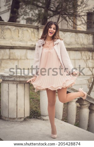 Happy woman dressed in a very sexy short nude dress and a warm coat with rose posing on one foot