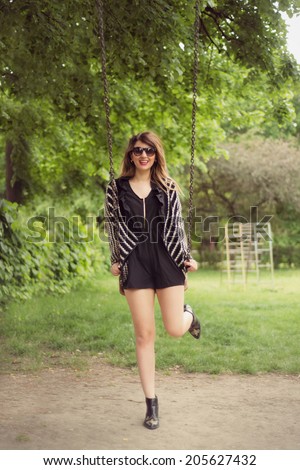 Fashion shoot of sexy woman posing on a leg between swings outdoor in a black romper jumpsuit