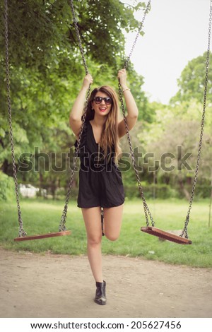 Fashion shoot of sexy woman posing outdoor in a black romper jumpsuit hanging on two swings