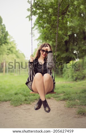 Fashion shoot of sexy woman swinging outdoor in a black romper jumpsuit
