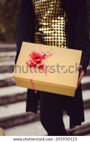 Young fashion lady in a sexy gold dress giving a gift in a sparkle golden box with red bow