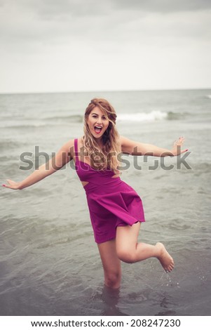 Fashion blonde happy portrait at the beach sea side posing in water dressed in a sexy fuchsia pink dress