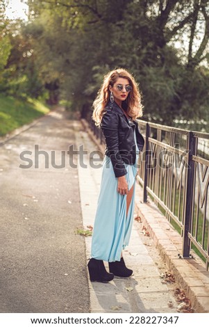 Gorgeous blonde posing in a sexy light blue dress tight and fluid on her body. Fashion shoot of beautiful woman at the river side with sun in her  hair