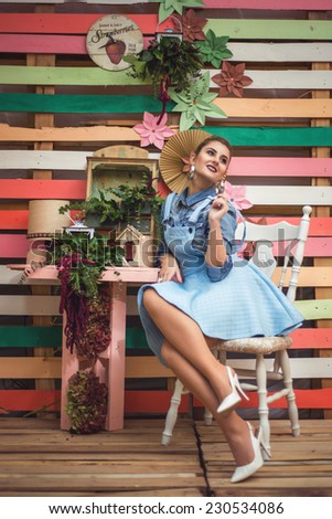 Colorful decor Studio Shot of Fashion Woman. Vivid Colors. Rainbow Colors painted on wood. Vintage objects. Beauty Girl Portrait wearing baby blue dress and seating
