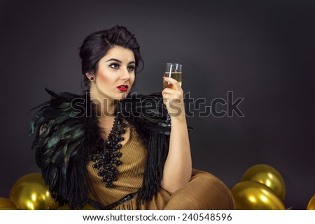 Happy fashion woman drinking champagne, dressed in a gold dress and feathers collar, surrounded with yellow balloons . New Year\'s Eve Party