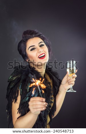 Happy fashion woman drinking champagne, holding fireworks dressed in a gold dress and feathers collar. New Year\'s Eve Party