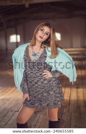 Fashion woman wearing baby blue baseball jacket over sexy knitted dress. Model posing in old attic with over-knee boots