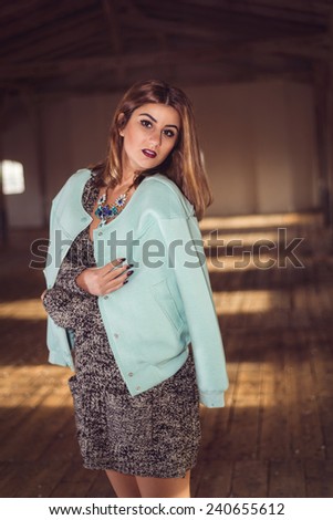 Fashion woman wearing baby blue baseball jacket over sexy knitted dress. Model posing in old attic