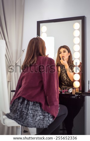 Reflection of young beautiful woman applying her make-up, looking in a mirror. Focus in the mirror