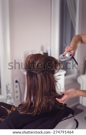 Hairstylist applying hair spray while arranging it