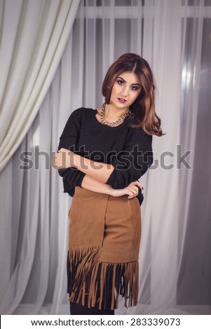 Studio portrait of beautiful woman dressed with a knitted black sweater and a brown skirt with fringes. Professional make-up and haistyle