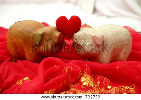 Two lovely smiling wooden pigs facing each other holding up a soft heart for Valentines