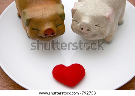 Two lovely smiling wooden pigs facing a soft heart for Valentines on a white platform