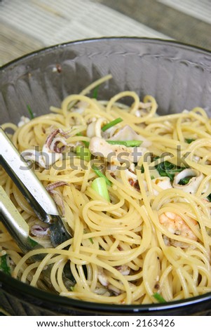 Seafood pasta with green leafy vegetables in a deep glass bowl