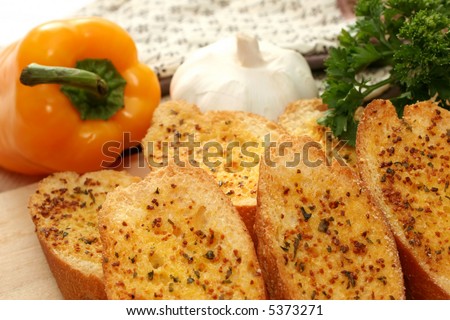 Toasted garlic bread on a wooden tray with yellow capsicum, garlic and parsley.
