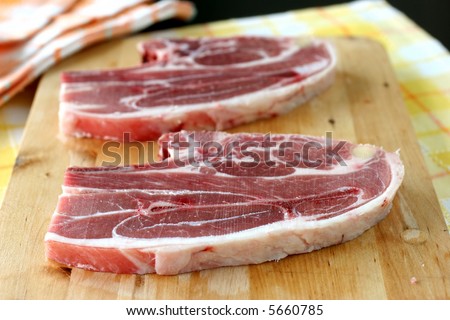 Two large cuts of raw Australian lamb cuts on a wooden chopping board in kitchen