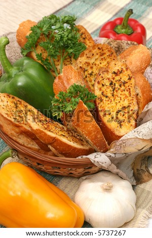 Garlic bread in a basket surrounded with colored peppers, garlic and parsley