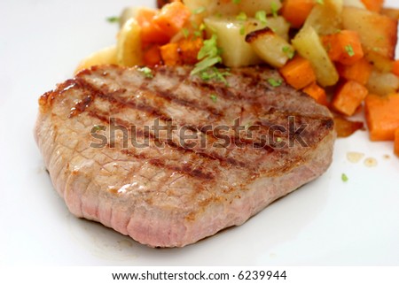 A round eye steak fried on a grilling pan with a serving of mixed cubed vegetables