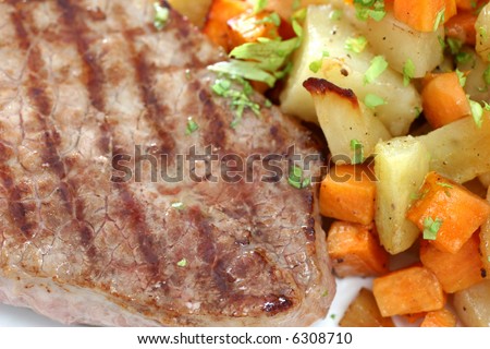 A round eye steak fried on a grilling pan with a serving of mixed cubed vegetables
