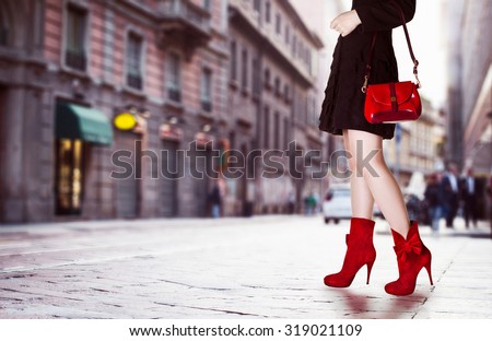 A girl with red bag and red boots in the street. Black coat.Beautiful legs in autumn winter time.