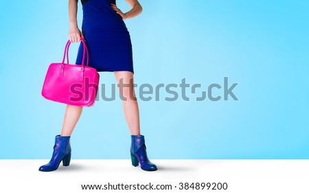 Beautiful legs woman with blue boots and pink bag. Isolated on blue with copy space. Fashion shopping image.