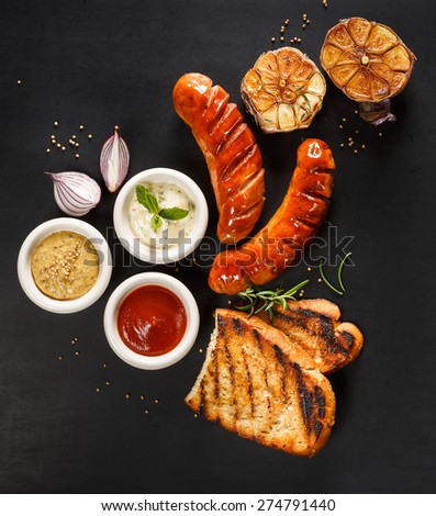 Grilled sausage with different kinds of dips on a black background