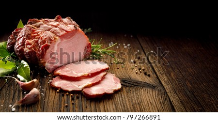 Sliced smoked gammon on a wooden  table with addition of fresh  herbs and aromatic spices.   Natural product from organic farm, produced by traditional methods
