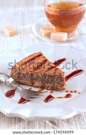 Chocolate and almond cake with caramel sauce, fork and sweet tea in transparent cup. On vintage brown plate and on natural pastel napkin with sugar pieces. Vertical.