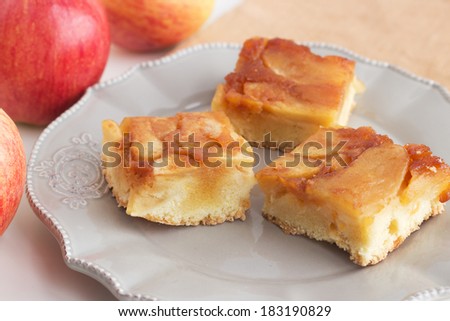 Traditional Russian charlotte apple cake with caramel on golden napkin and apples on the background. Cut in squares.