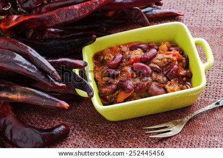 Traditional mexican chili con carne: chilly with mixed meat, beans and tomatoes with dry hot papers on the background.