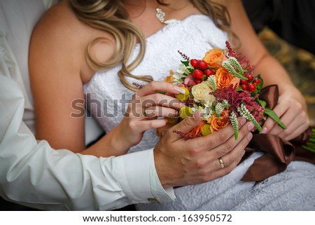 hands of the bride and groom with rings on a beautiful wedding bouquet
