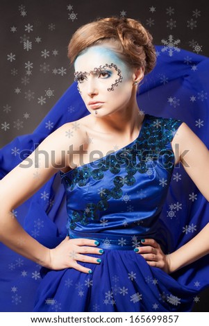 Creative winter portrait of a beautiful woman. Fashion style. Blue long dress and snowflakes. Queen of snow.