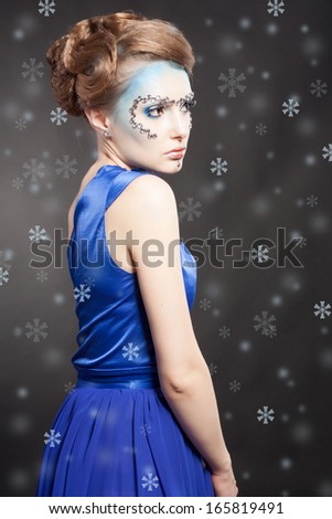 Portrait of winter cold woman with snow splash. Christmas girl. Beauty model lady. Winter makeup. Blue fluttering dress.