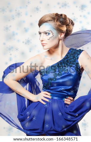 Portrait of winter cold woman with snow splash. Christmas girl. Beauty model lady. Winter makeup and hairstyle. Blue fluttering dress. Snow queen.