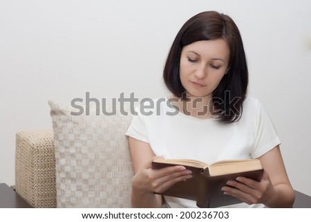 Happy young woman reading a book on couch at home