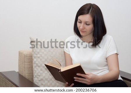 Happy young woman reading a book on couch at home